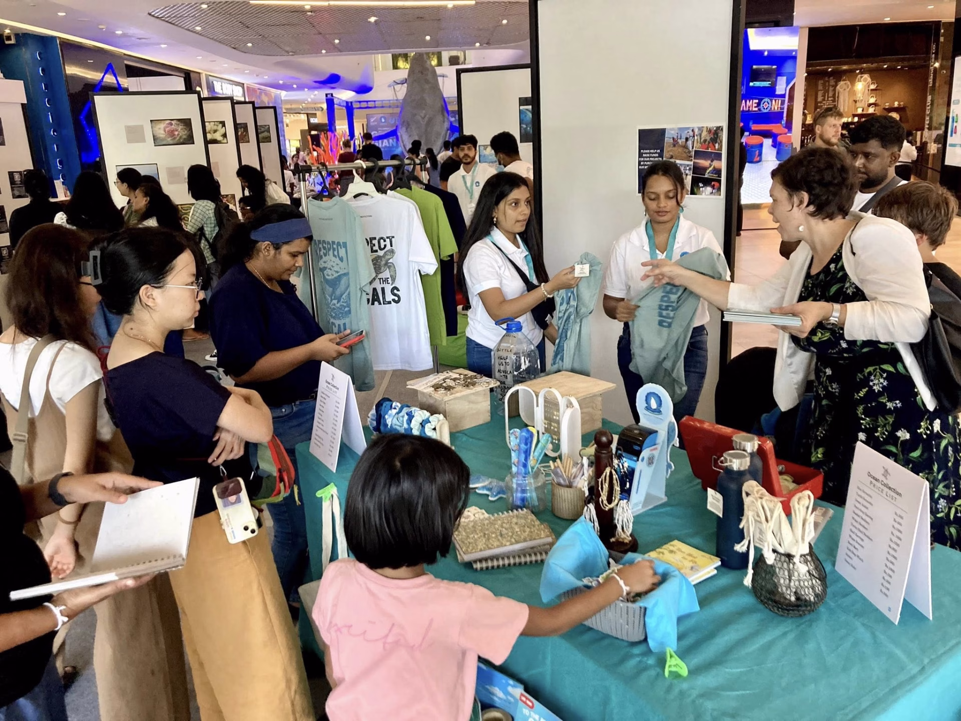 Volunteers engage with the public at a merchandise and education table featuring ocean-themed sustainable products.