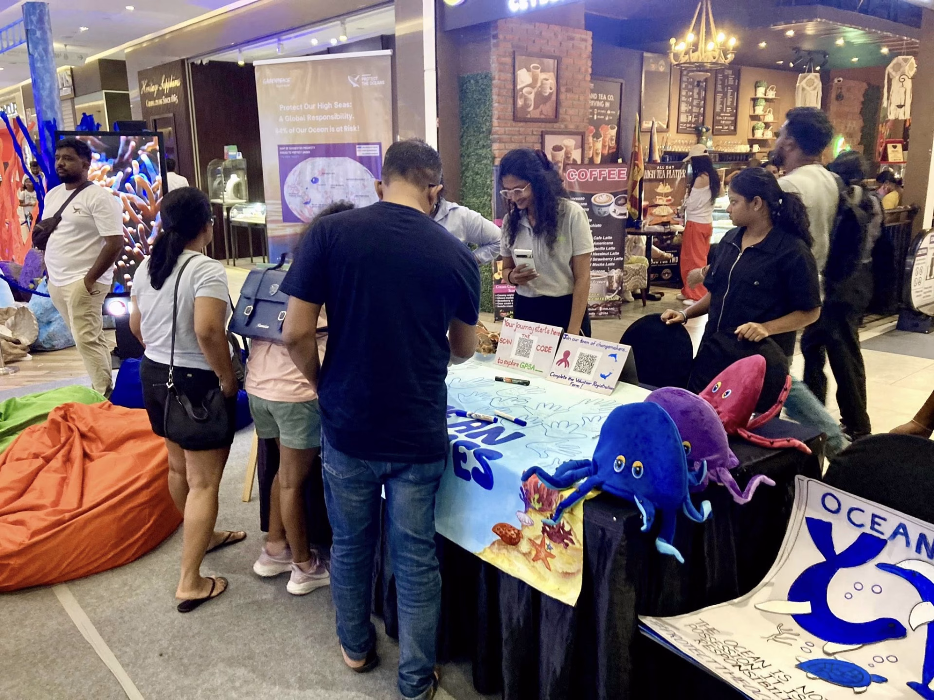 Children and adults signing banners and interacting with plush sea creatures at a vibrant, ocean-themed awareness booth.