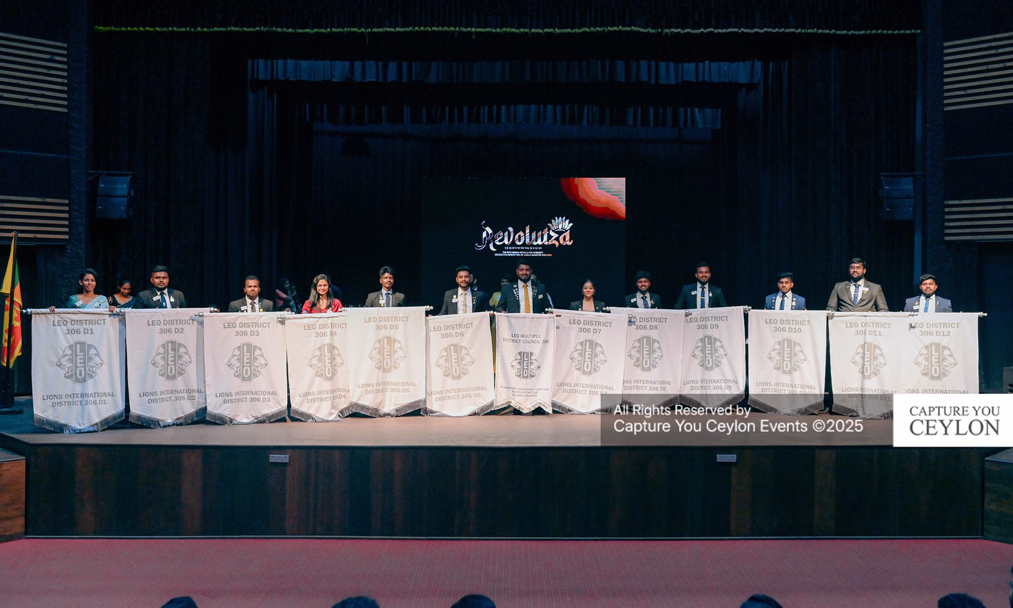 Leaders of Leo Multiple District 306 seated on stage with banners of the twelve newly formed Leo Districts during the Revolutza 2025 Installation Ceremony in Colombo.